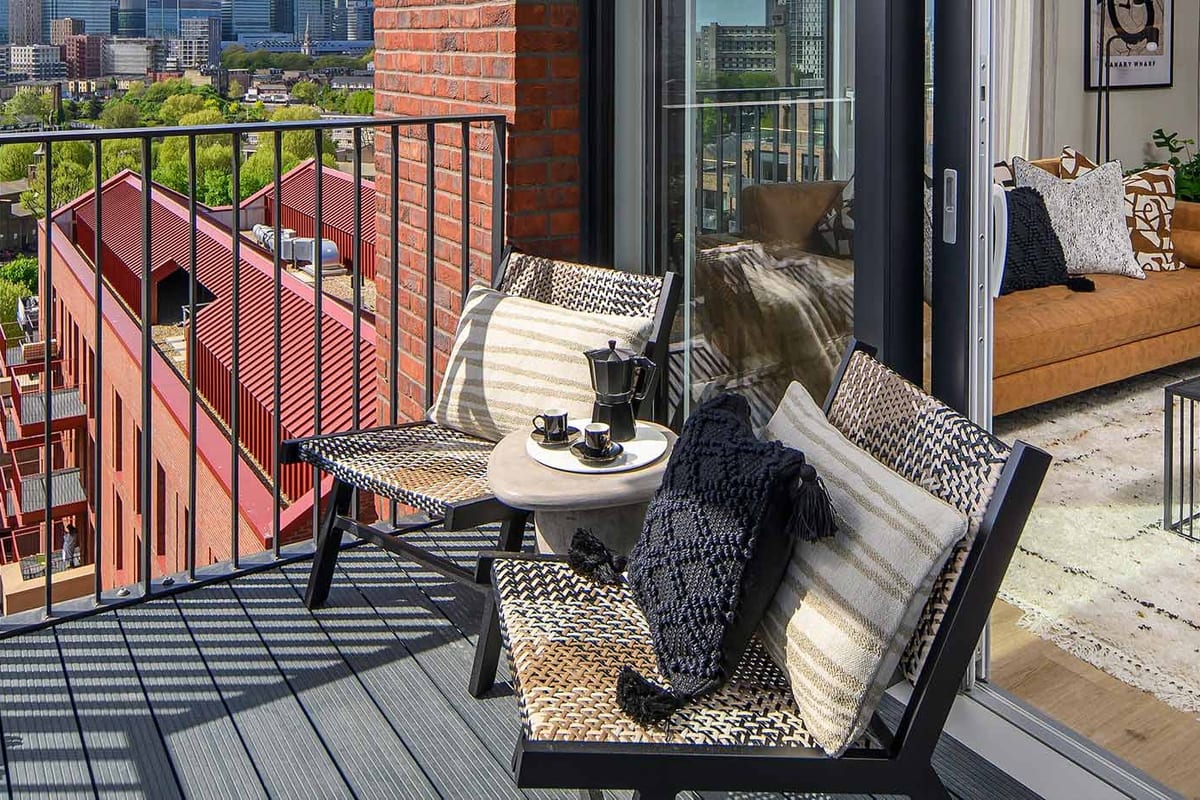 Balcony with woven chairs and a side table, looking over red-brick rooftops to the Canary Wharf skyline