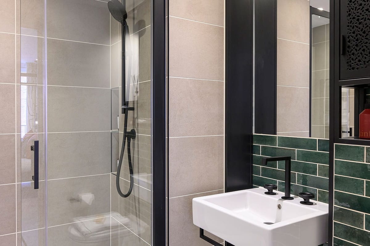 Shower room with a glass screen, matt black fittings and green glazed tiles behind a white basin