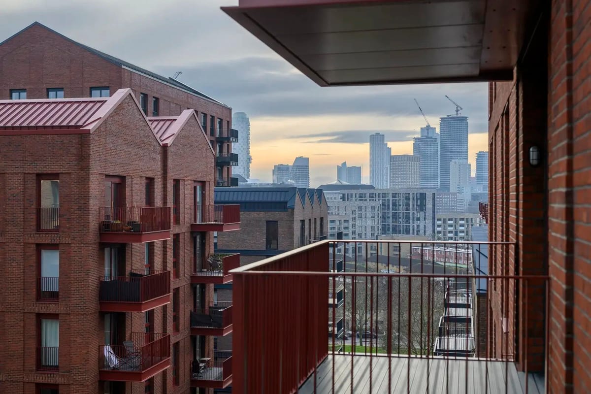 Balcony at dusk looking past red-brick buildings to the lit towers of Canary Wharf