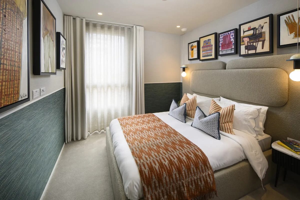 Bedroom with an orange patterned throw, teal tiled dado and a row of framed prints above the bed