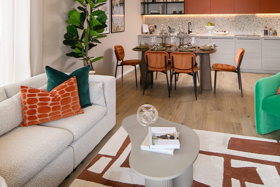Living room with a cream sofa, terracotta and teal cushions, a green velvet armchair and a geometric rug, the dining table beyond