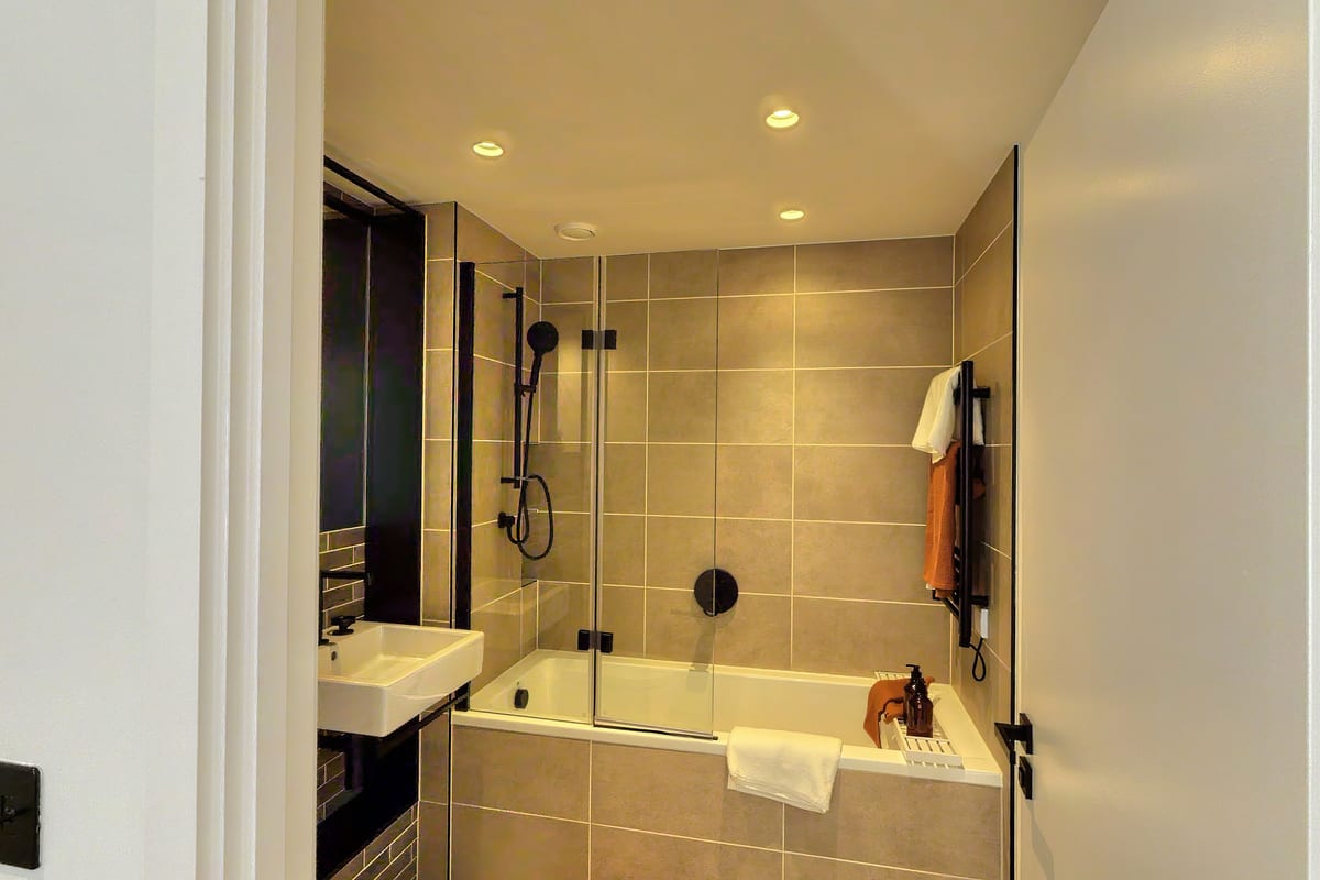 Bathroom with large grey tiles, a bath with a black-framed glass screen and matt black shower fittings
