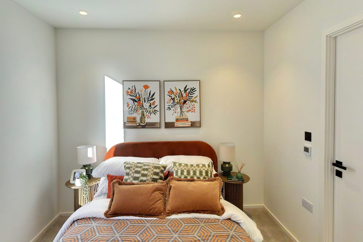Bedroom seen head-on: a curved rust velvet headboard beneath two botanical prints, bedside lamps and orange cushions