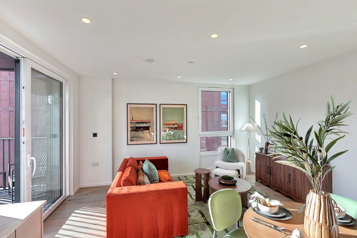 Living room with a red velvet sofa beneath two framed prints, a walnut sideboard, a cream armchair and sliding doors to the balcony