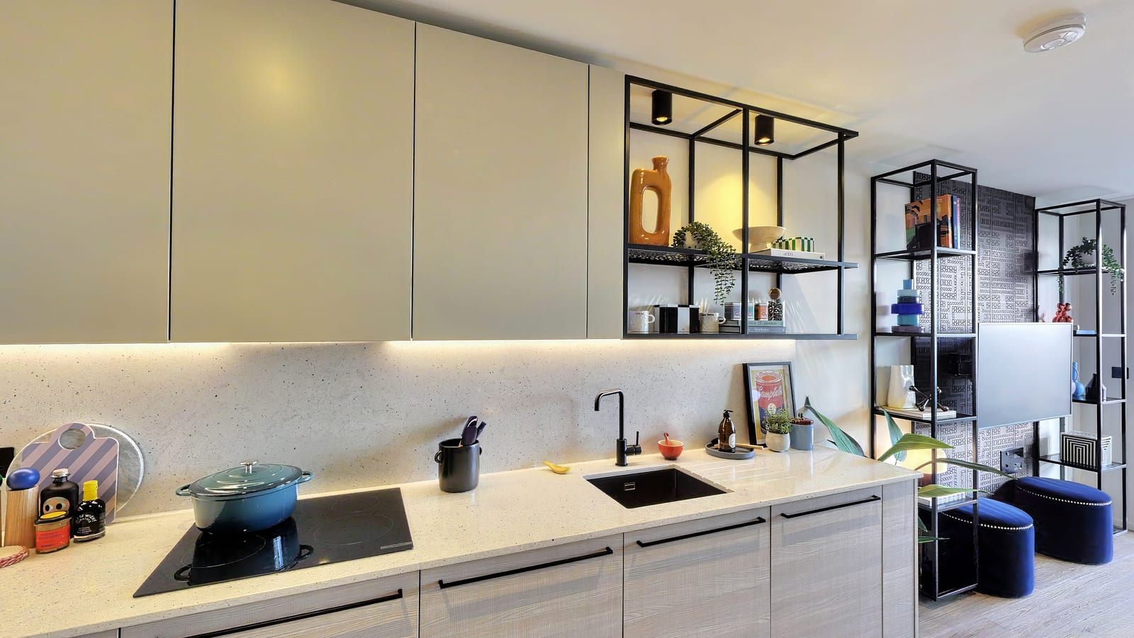 Kitchen in The Millhouse show apartment: pale units with a terrazzo worktop, black open shelving styled with ceramics, and blue velvet stools by the living area