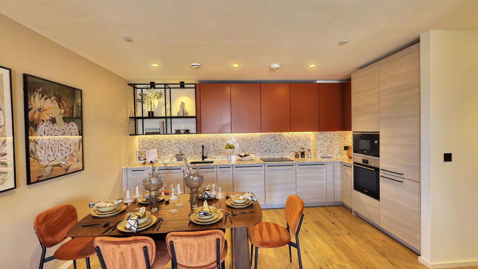 Kitchen and dining area in apartment B1-04-06: terracotta wall units, a terrazzo splashback and black open shelving above a walnut table laid with orange chairs